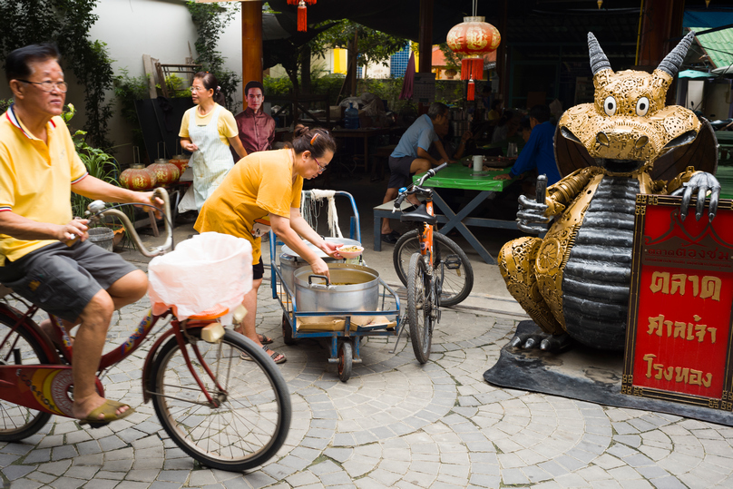 Residents moving through San Chao Rong Thong Market beside shrine art