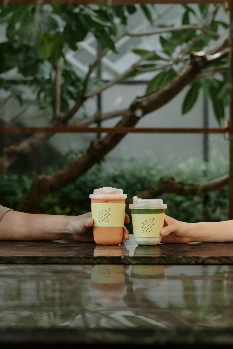 Two Cafe LOM takeaway cups held in the garden