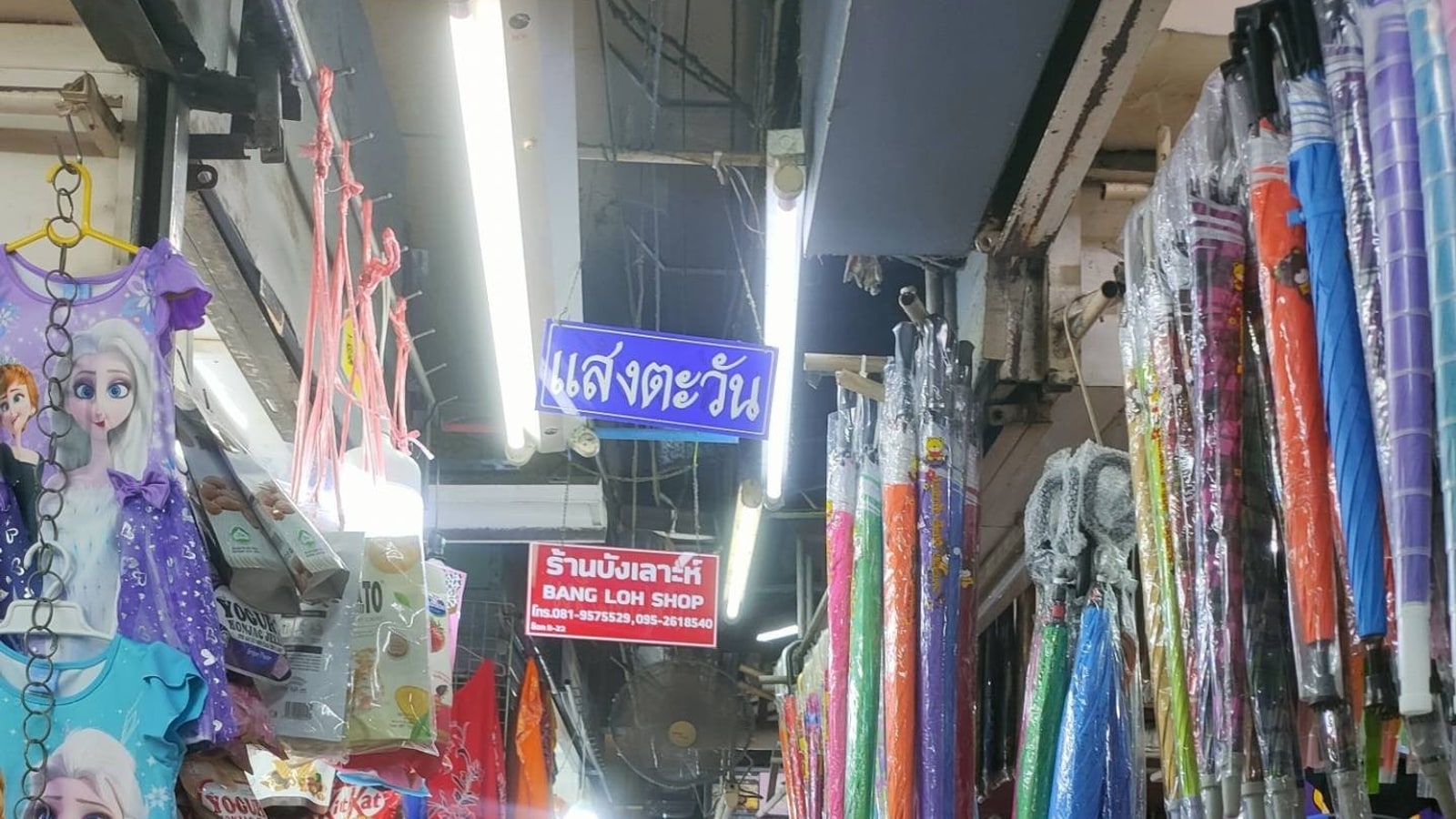 Covered market aisle with textiles and shop signs at Kim Yong Market